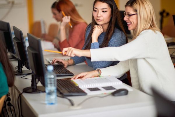 Two women looking at a screen together. One woman is pointing something out to the other woman